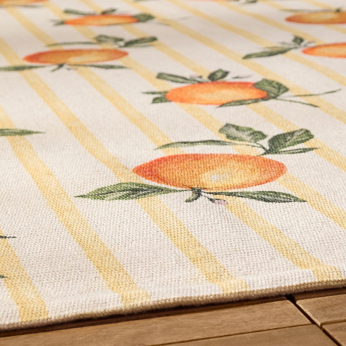 Close-up of the Fruits Gingham Polyester Rug in yellow, showing a hand-painted orange print with green leaves over soft yellow stripes on a cream polyester ground.