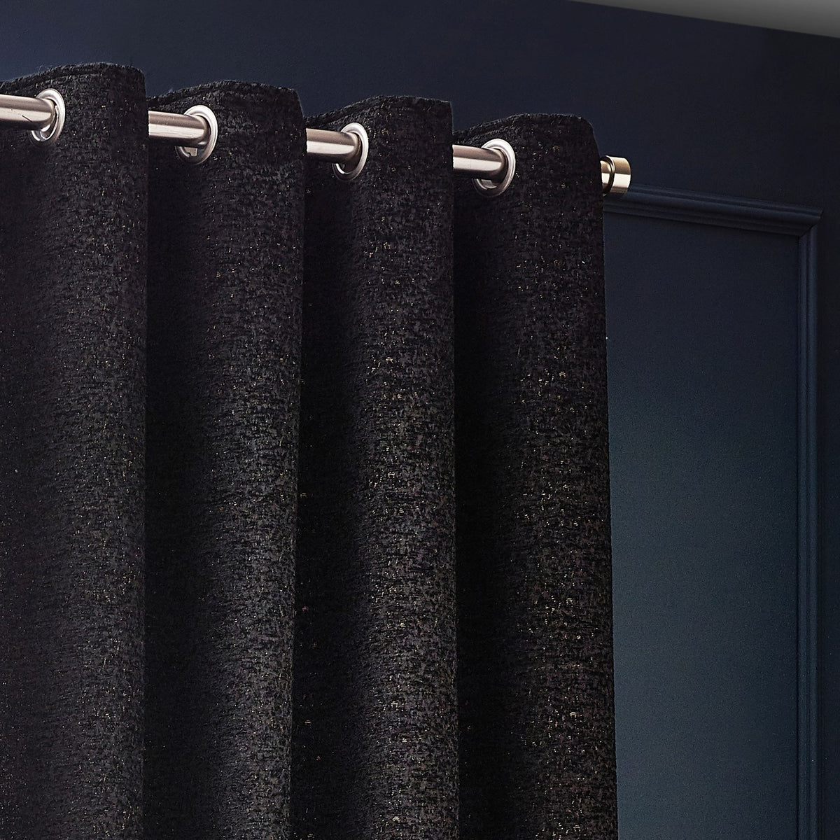 Galaxy Chenille fully lined eyelet curtains in black with gold flecks, shown close-up on brushed metal grommets and a pole against a dark wall.