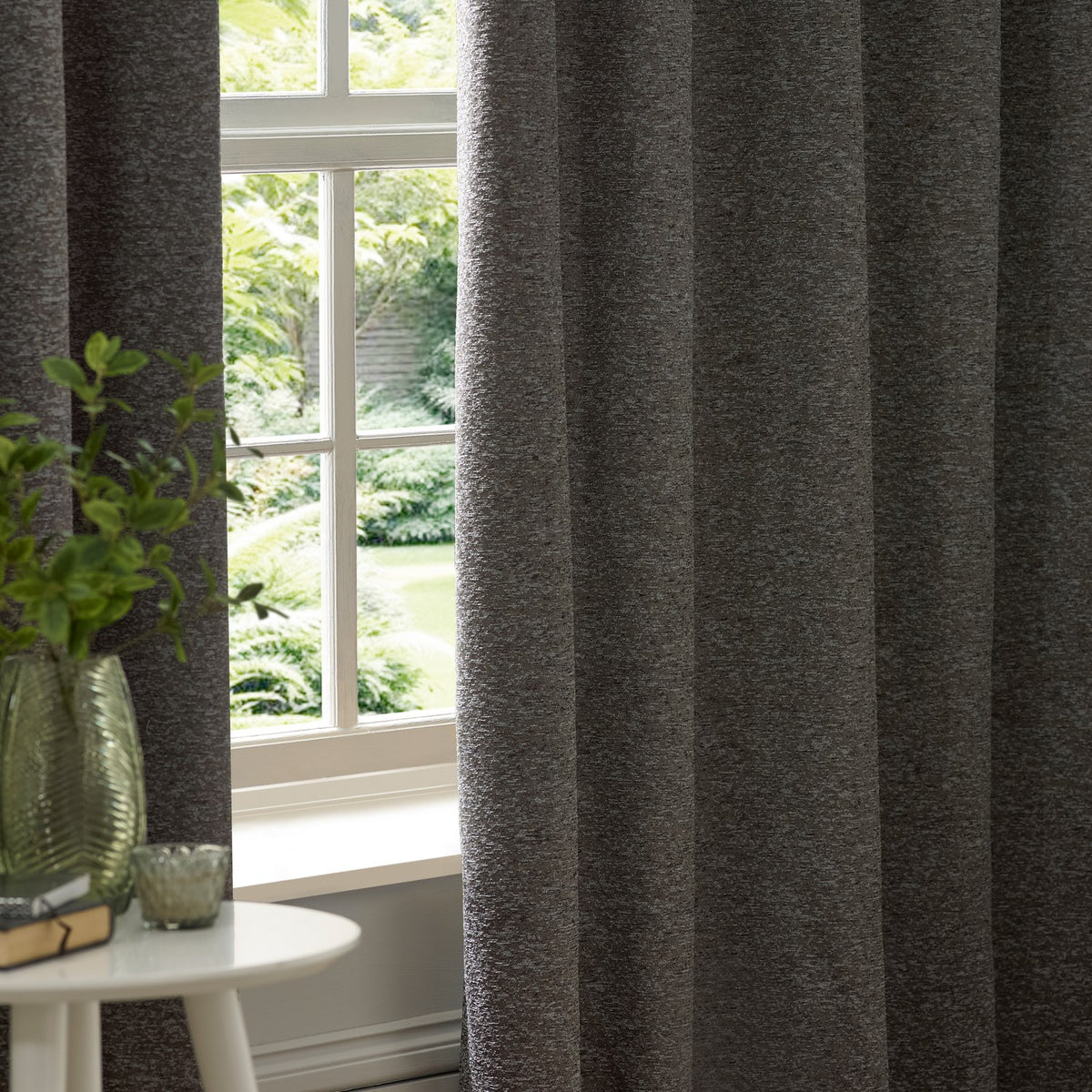 Galaxy Chenille Fully Lined Eyelet Curtains in charcoal hanging beside a window, showing the textured chenille fabric with eyelet heading in a living room setting.