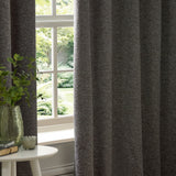 Galaxy Chenille Fully Lined Eyelet Curtains in charcoal hanging beside a window, showing the textured chenille fabric with eyelet heading in a living room setting.