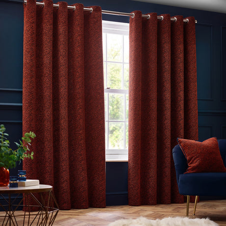 Galaxy Chenille Fully Lined Eyelet Curtains in copper, textured rust-toned fabric with silver eyelet heading, hung on a pole in a navy-walled living room beside a window.