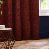Galaxy Chenille Fully Lined Eyelet Curtains in copper, hung at a window in a living room with dark blue panelling and wood flooring, showing textured rust-toned fabric with golden flecks.
