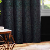 Galaxy Chenille Fully Lined Eyelet Curtains in Emerald, shown in soft folds by a window in a living room with wooden flooring and a round side table.