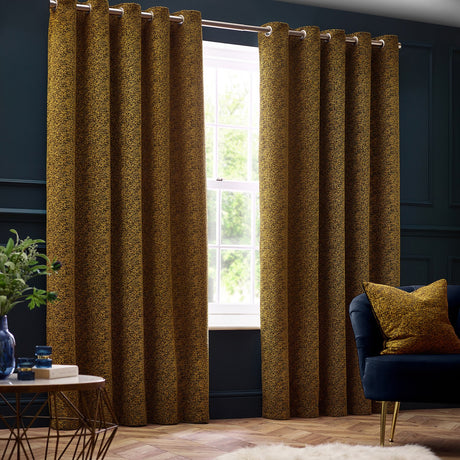 Galaxy Chenille Fully Lined Eyelet Curtains in gold, mottled textured fabric hung from a rail in a dark-walled living room with a matching cushion on a navy sofa.