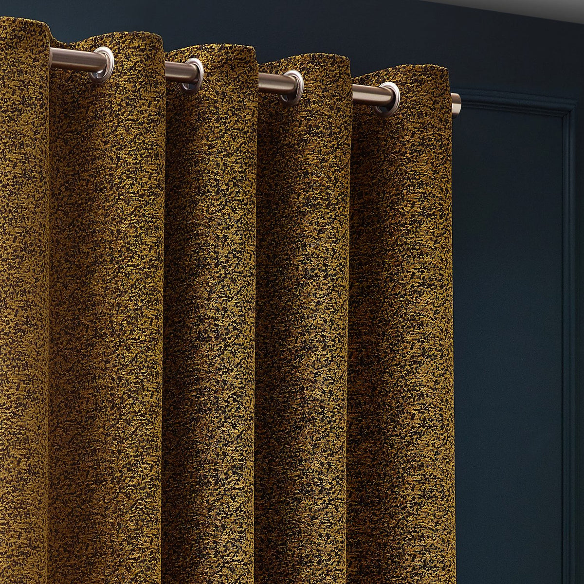 Galaxy Chenille Fully Lined Eyelet Curtains in Gold, showing mottled woven texture with metal eyelets on a chrome pole against a dark blue wall.