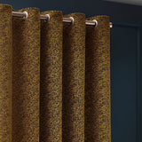 Galaxy Chenille Fully Lined Eyelet Curtains in Gold, showing mottled woven texture with metal eyelets on a chrome pole against a dark blue wall.