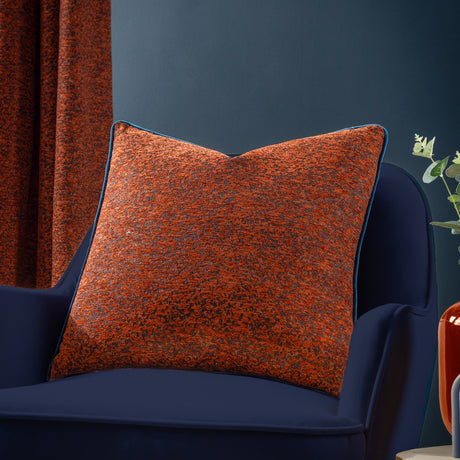Galaxy Eyelet Chenille Cushion in Copper, a square cushion with textured rust-orange chenille fabric and teal piping, shown on a navy velvet chair.