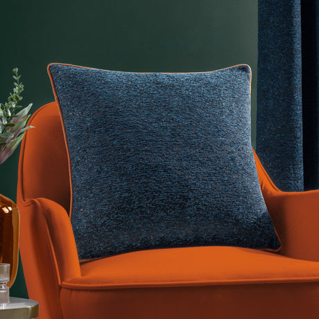 Galaxy Eyelet Chenille Cushion in navy with orange piped edge, shown on an orange velvet armchair against a dark green wall.