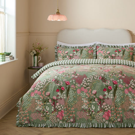 Gardenia Reversible Botanical Duvet Cover Set in Pink Forest, shown on a bed with ruffle-edged pillow shams in a pink and green floral print over a sage ground, in a bedroom setting.