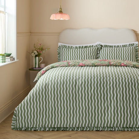 Gardenia Reversible Botanical Duvet Cover Set in Pink Forest on a bed, showing green and white wavy stripe side with ruffled edges and floral-print reverse peeking at the pillow shams.