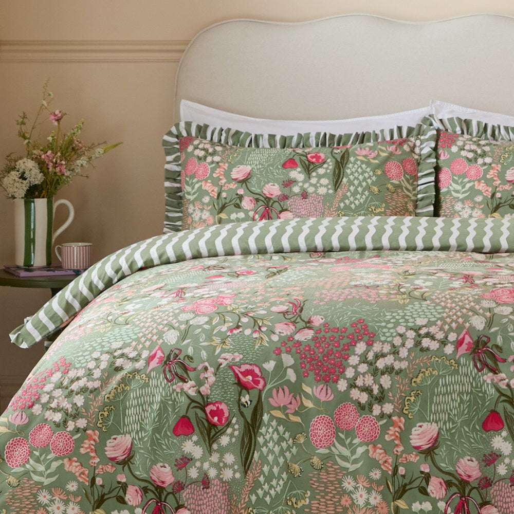 Gardenia Reversible Botanical Duvet Cover Set in Pink Forest, shown on a bed with pink and cream floral print on sage green, ruffled pillow shams, and green wavy-striped reverse.