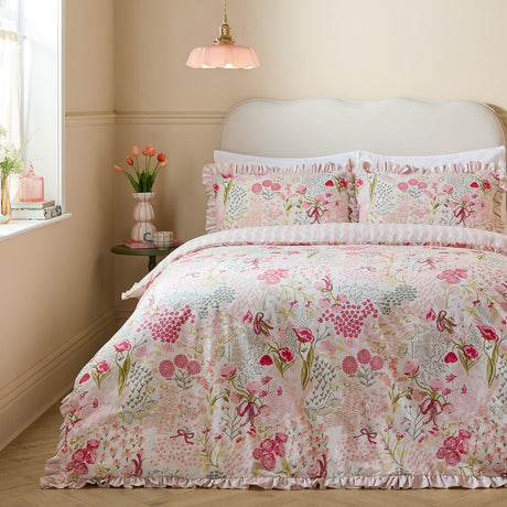 Gardenia Reversible Botanical Duvet Cover Set in Pink Pebble on a bed with frilled edging, floral print in pink and sage tones, styled in a soft pink bedroom.