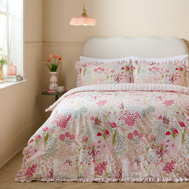 Gardenia Reversible Botanical Duvet Cover Set in Pink Pebble on a bed with frilled edging, floral print in pink and sage tones, styled in a soft pink bedroom.
