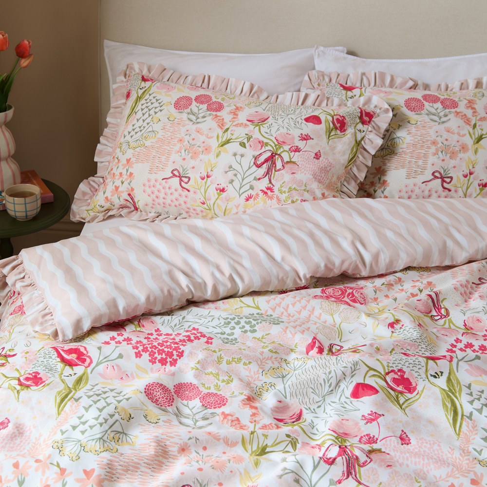 Gardenia Reversible Botanical Duvet Cover Set in Pink Pebble on a bed, floral pink and sage print with frilled edge, reverse side showing wavy pink and white stripe.
