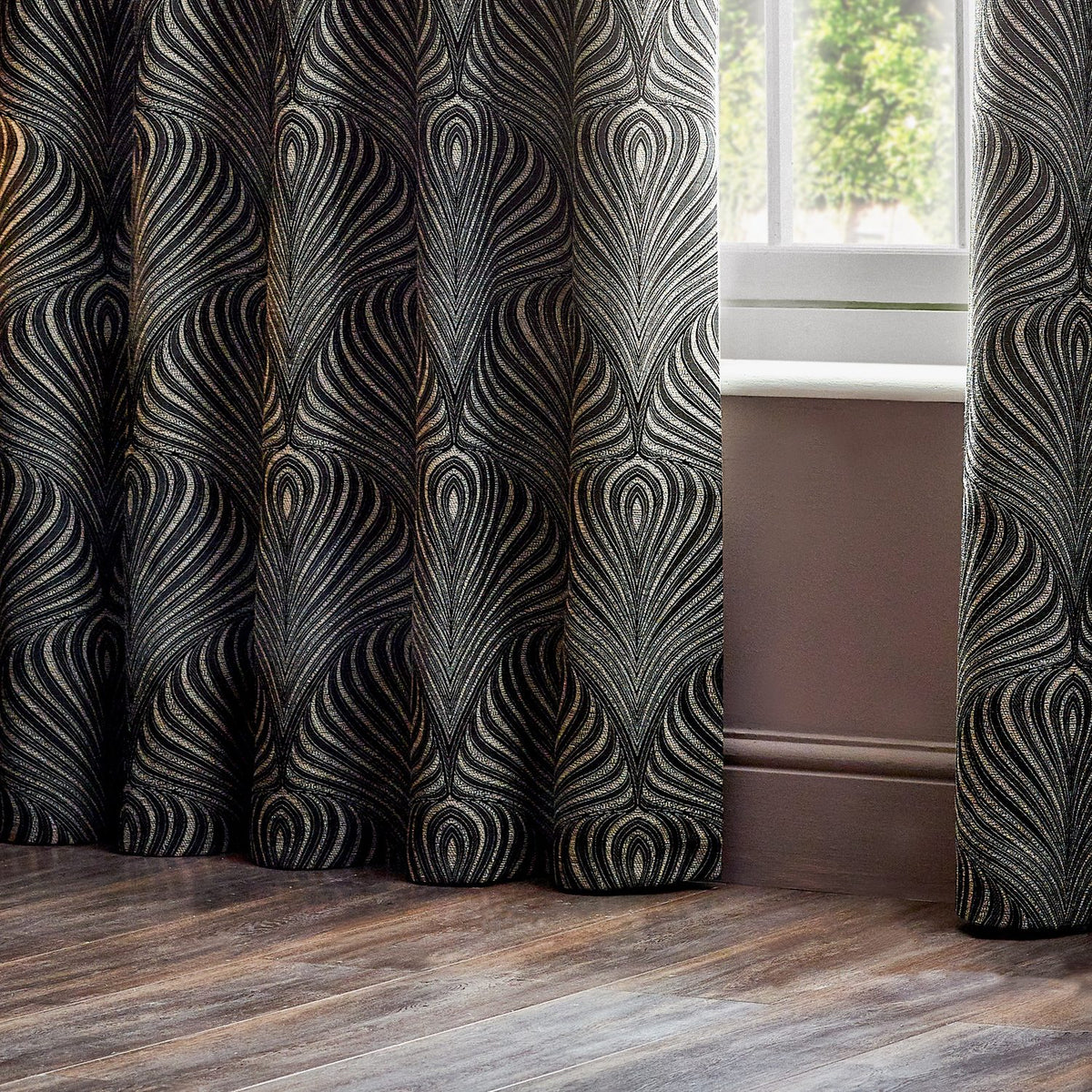 Gatsby Jacquard Lined Eyelet Curtains in black, showing a flowing feathered Art Deco pattern in champagne and gold jacquard fabric, styled beside a window in a room setting.