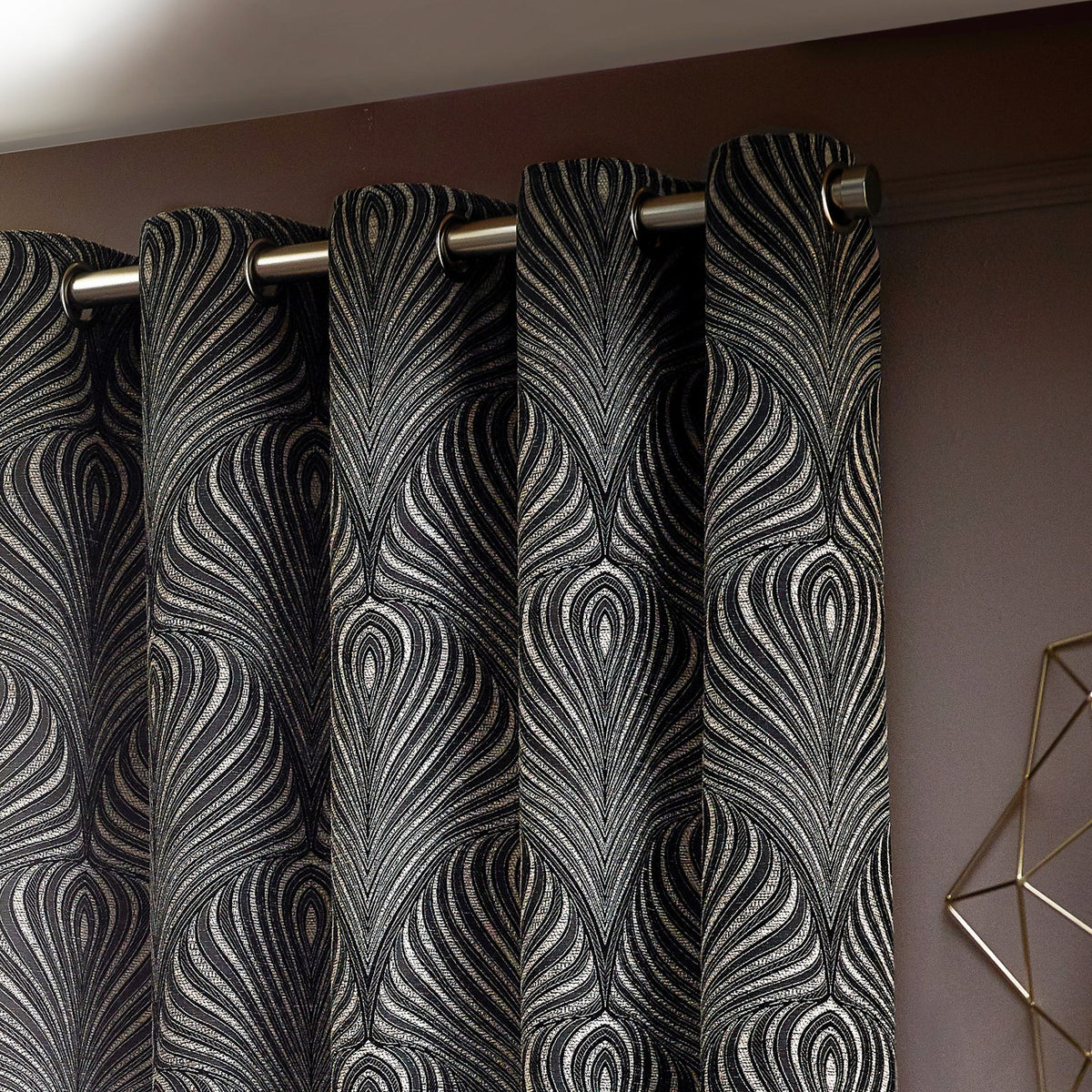 Gatsby Jacquard Lined Eyelet Curtains in black, showing feathered Art Deco-style pattern in champagne and gold tones, hung on a metal pole with eyelet fittings.