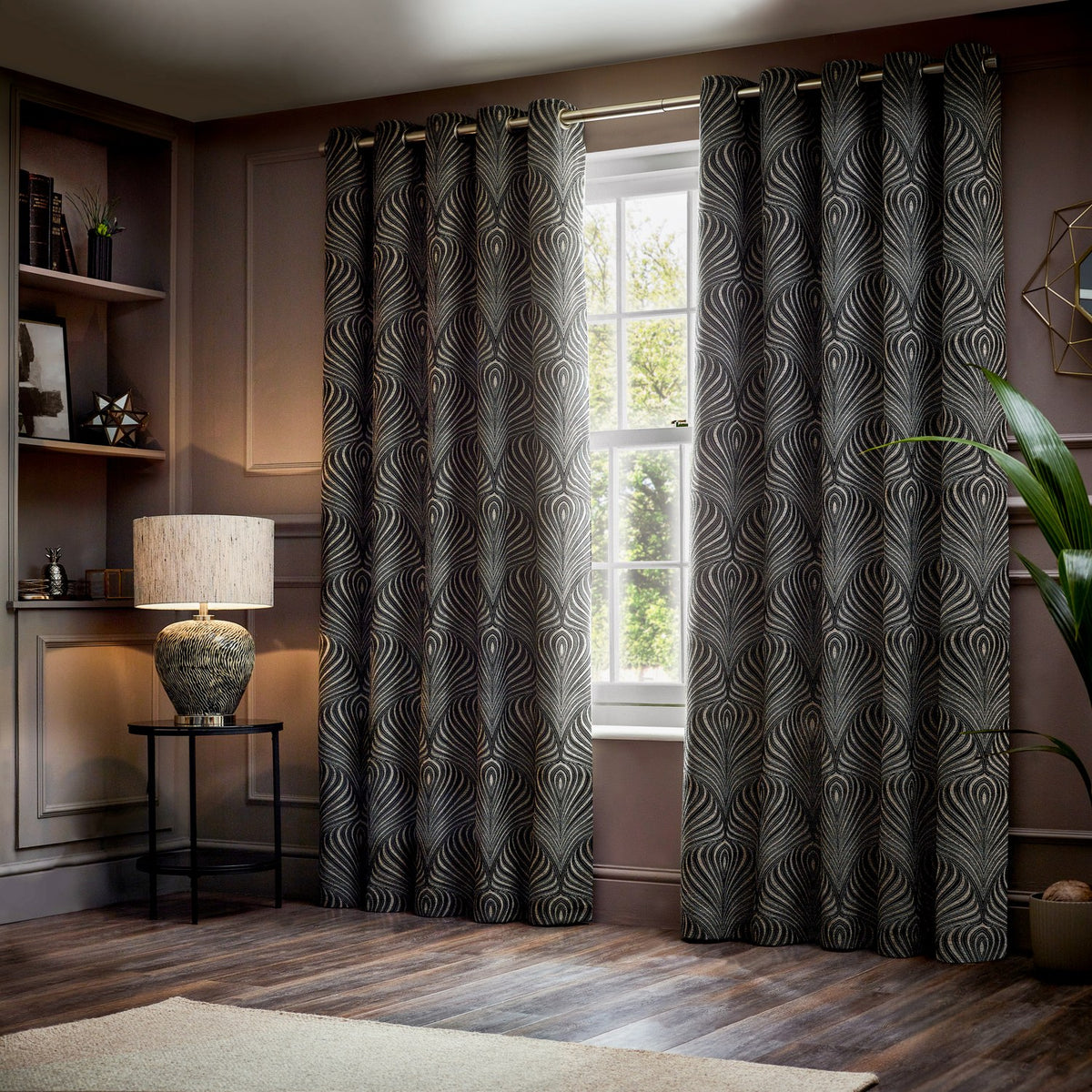 Gatsby Jacquard Lined Eyelet Curtains in black with champagne and gold feathered arc pattern, hung either side of a window in a living room setting.