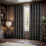 Gatsby Jacquard Lined Eyelet Curtains in black with champagne and gold feathered arc pattern, hung either side of a window in a living room setting.