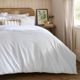 Georgia Woven Polycotton Duvet Cover Set in white, styled on a bed with textured raised pattern, ruffled and striped cushions, in a bedroom with rattan headboard.