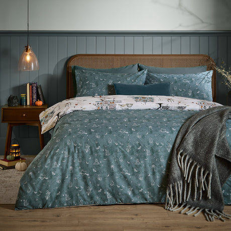 Ghost Town Reversible Woodland Duvet Cover Set in Dusk blue on a bed with cane headboard, showing cream ghost-motif reverse peeking at the pillows, styled in a moody bedroom.