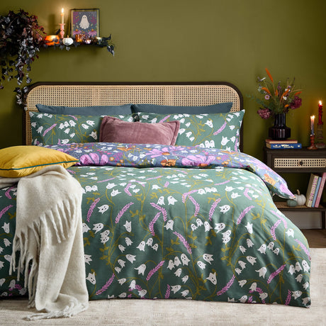 Ghoul Gardens reversible duvet cover set on a bed, showing the sage-green ghost and lavender print with matching pillowcases in a green-walled bedroom.