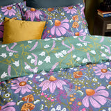 Ghoul Gardens reversible duvet cover on a bed, slate-blue floral ghost print with pink coneflowers folded back to reveal the sage-green ghost and lavender reverse side.