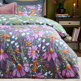 Ghoul Gardens reversible duvet cover set on a bed, slate-blue side with pink coneflowers, orange toadstools and ghosts, paired with a sage-green ghost print pillowcase.