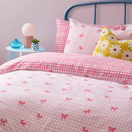 Gingham Bows Reversible Check Duvet Cover Set in pink, styled on a bed with matching pillowcase and gingham cushion beside a yellow floral cushion.