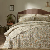 Golden Lily quilted cotton bedspread in natural and gold floral print, shown folded on a bed with matching pillowcases in a bedroom setting.