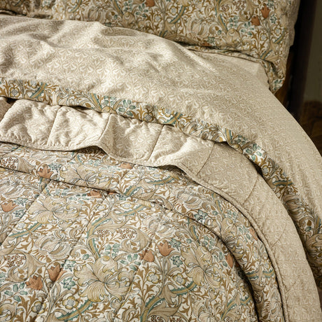 Golden Lily quilted cotton bedspread in natural and gold, showing the floral face fabric folded back to reveal the tonal damask-style reverse and matching pillowcase trim.