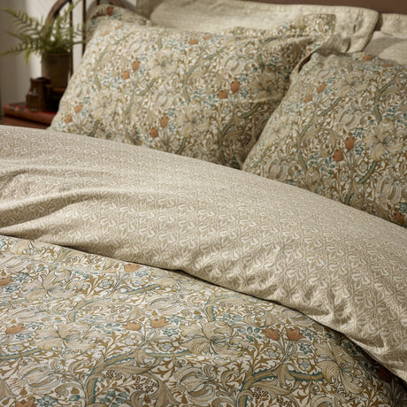 Golden Lily cotton duvet cover set with pillowcases, showing a floral lily and tulip print in natural and gold tones on the bed, paired with a tonal damask-style reverse.