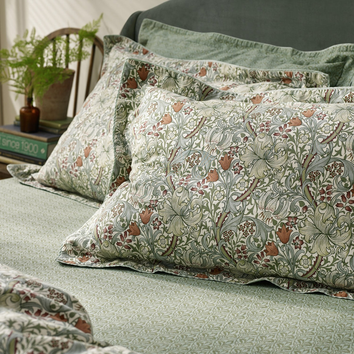 Golden Lily percale cotton pillowcase pair in Herbal Green, patterned with a classic Morris floral print, styled on a bed with matching sheets in a bedroom setting.