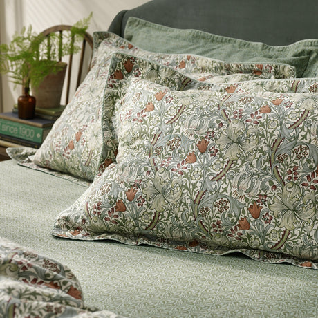 Golden Lily percale cotton pillowcase pair in Herbal Green, patterned with a classic Morris floral print, styled on a bed with matching sheets in a bedroom setting.