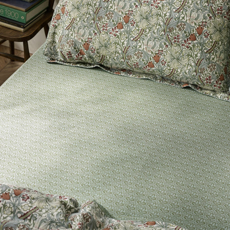 Golden Lily percale cotton fitted sheet in Herball Green, shown on a bed with a small leaf print, paired with matching floral-patterned pillowcases.