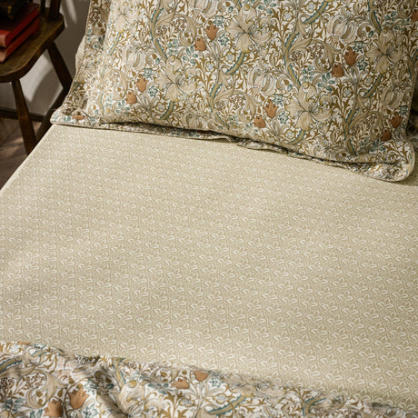 Golden Lily Percale Cotton Fitted Sheet in natural and sage green small-scale botanical trellis print, shown on a bed with a coordinating floral pillowcase.