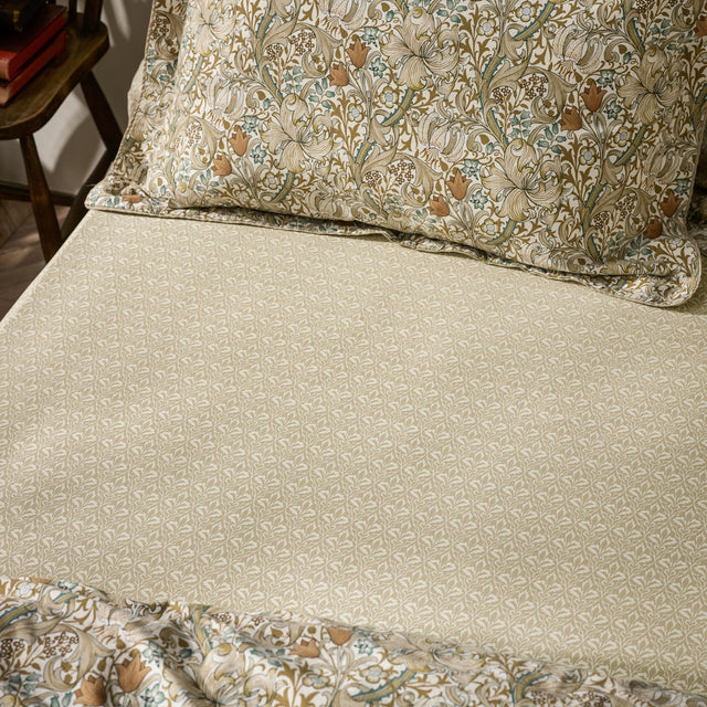 Golden Lily Percale Cotton Fitted Sheet in natural and sage green small-scale botanical trellis print, shown on a bed with a coordinating floral pillowcase.