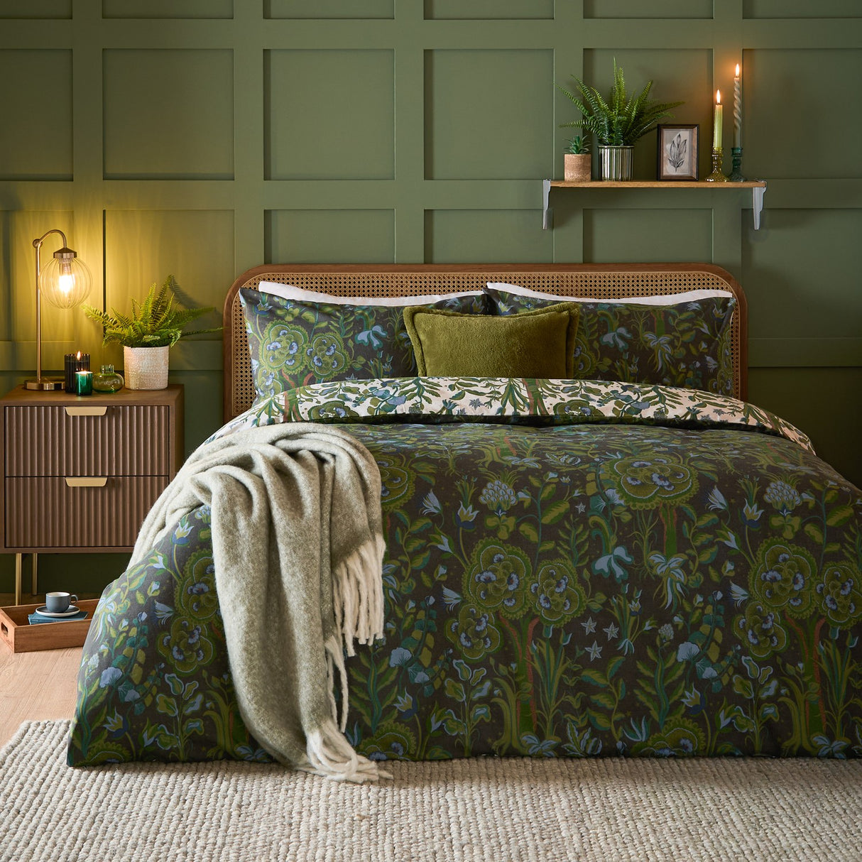 Garden of Wonder Reversible Floral Duvet Cover Set in Evergreen, shown on a bed with dark botanical print, green cushions and cream reverse, styled in a green-panelled bedroom.