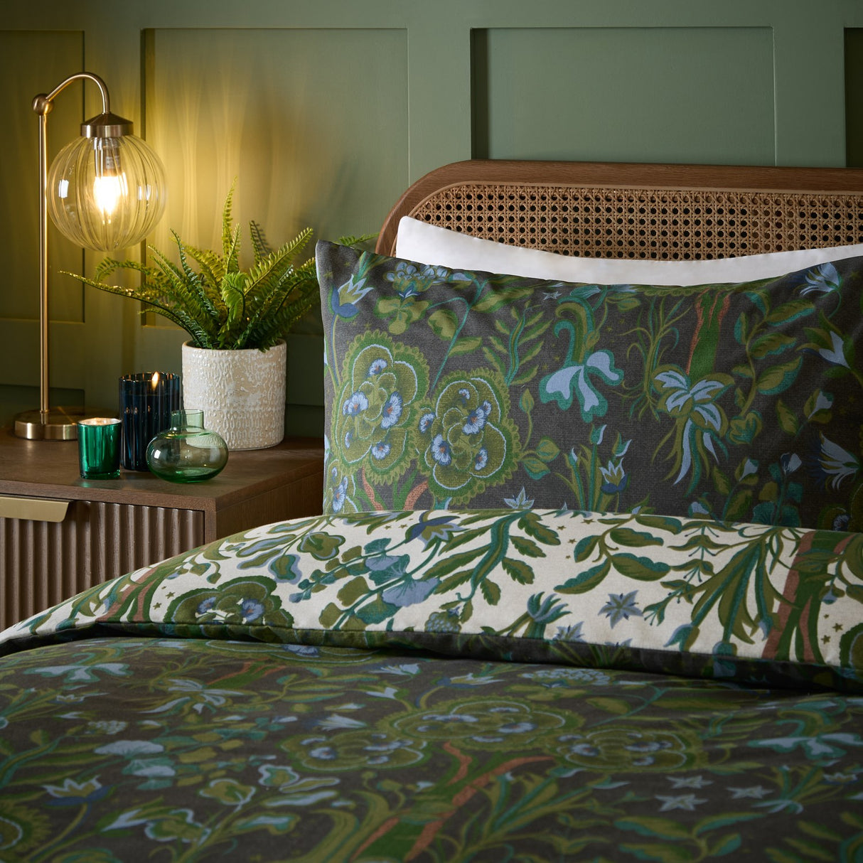 Garden of Wonder Reversible Floral Duvet Cover Set in Evergreen, shown on a bed with pillowcase, dark green ground with botanical print reversing to a cream floral side, in a bedroom setting.