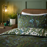 Garden of Wonder Reversible Floral Duvet Cover Set in Evergreen, shown on a bed with pillowcase, dark green ground with botanical print reversing to a cream floral side, in a bedroom setting.