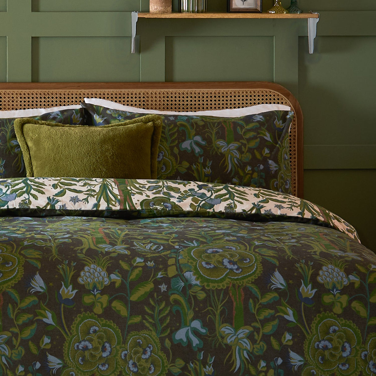 Garden of Wonder Reversible Floral Duvet Cover Set in Evergreen, shown on a bed with a dark green botanical print and a cream floral reverse edge, styled with a green cushion in a rustic bedroom.