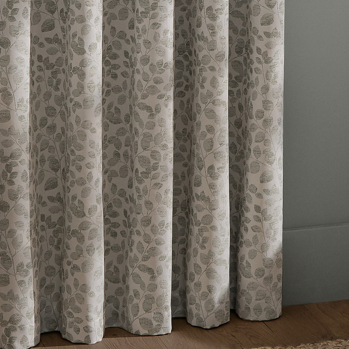 Grace Leaf Jacquard fully lined eyelet curtains in mist grey, showing folded panels with a woven trailing leaf pattern in soft grey on a paler ground.