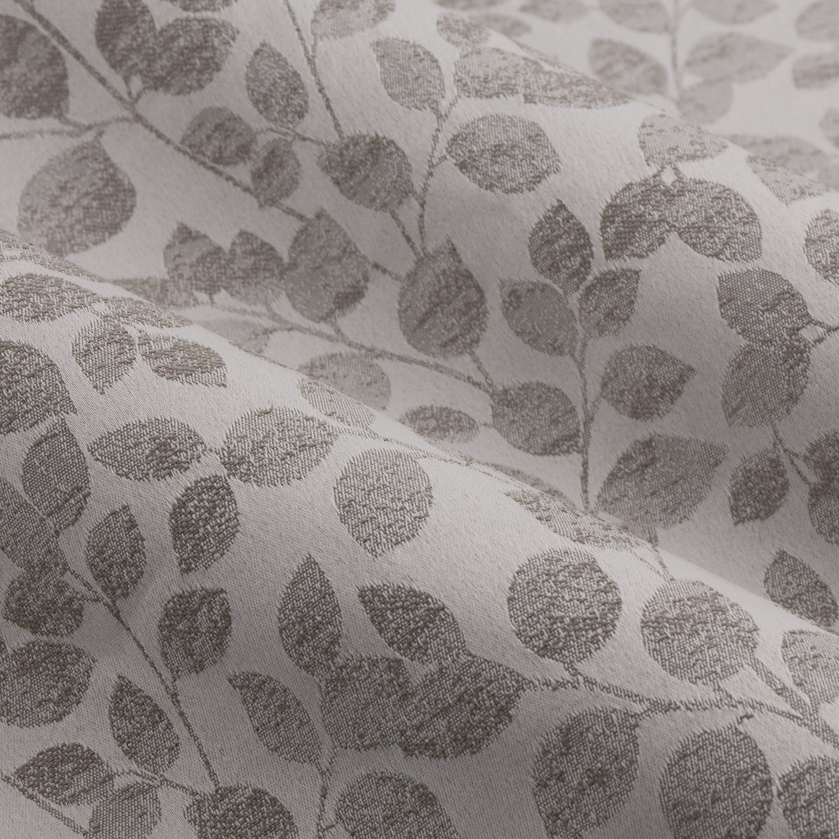 Close-up of Grace Leaf Jacquard eyelet curtain fabric in mist grey, showing a woven trailing leaf pattern in soft grey tones on a paler ground with textured jacquard weave.