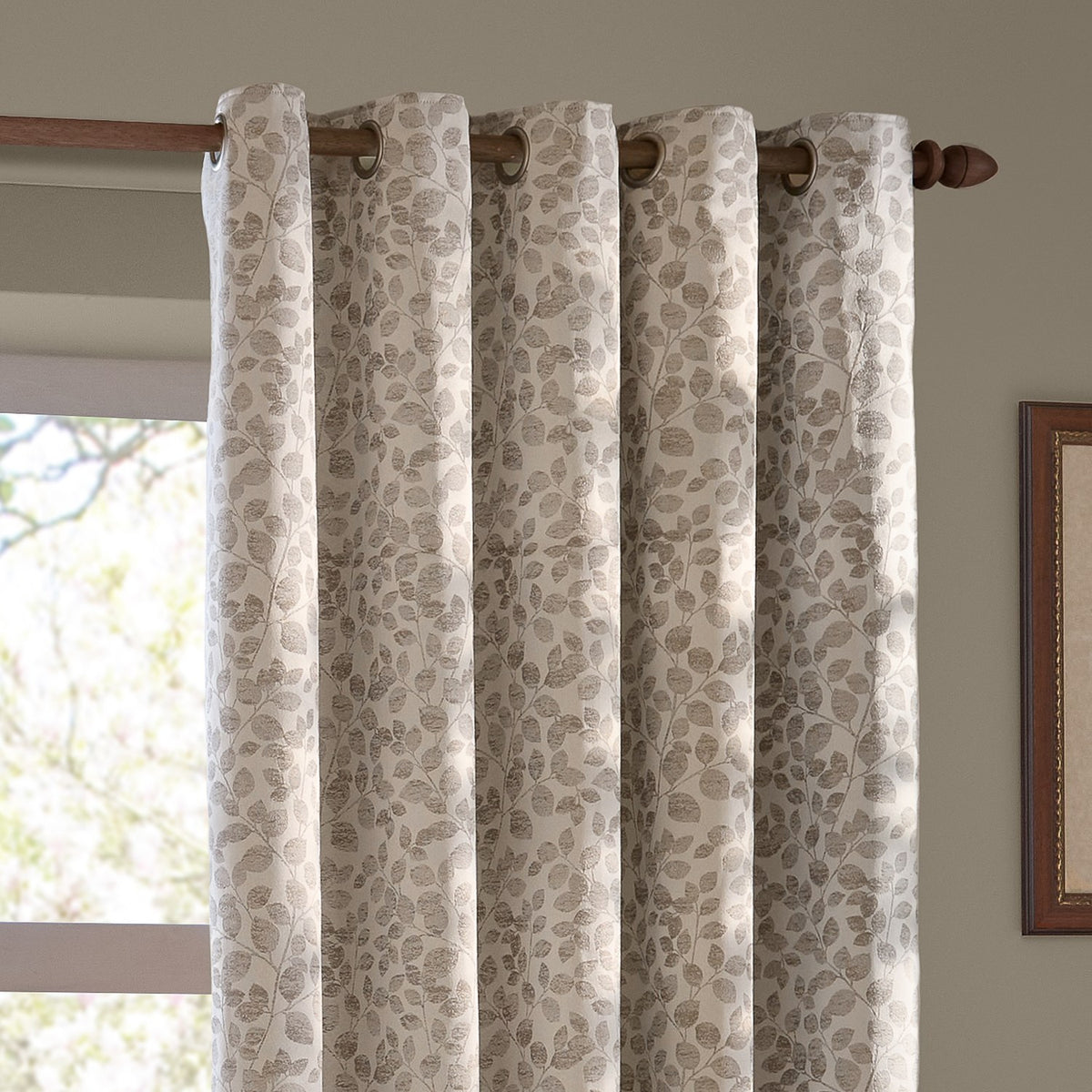 Grace Leaf Jacquard eyelet curtains in natural, showing woven leaf-branch pattern on a wooden pole with round eyelet rings, hung by a bright window.
