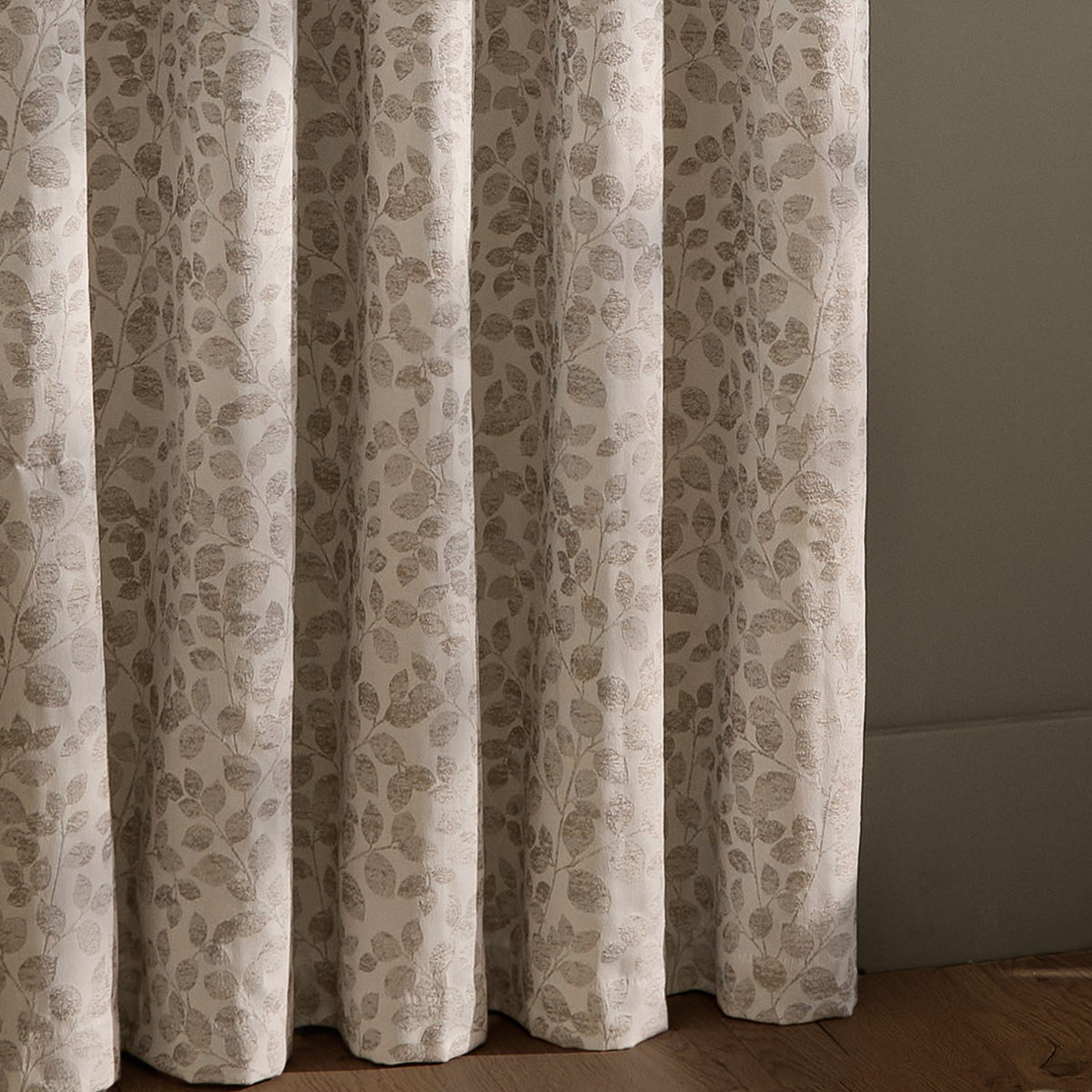 Grace Leaf Jacquard Fully Lined Eyelet Curtains in natural, showing floor-length folds with a woven leaf pattern in muted beige tones against a light wall.