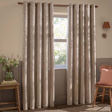 Grace Leaf Jacquard fully lined eyelet curtains in taupe with a tonal woven leaf pattern, shown hanging on a wooden pole beside a window in a living room setting.