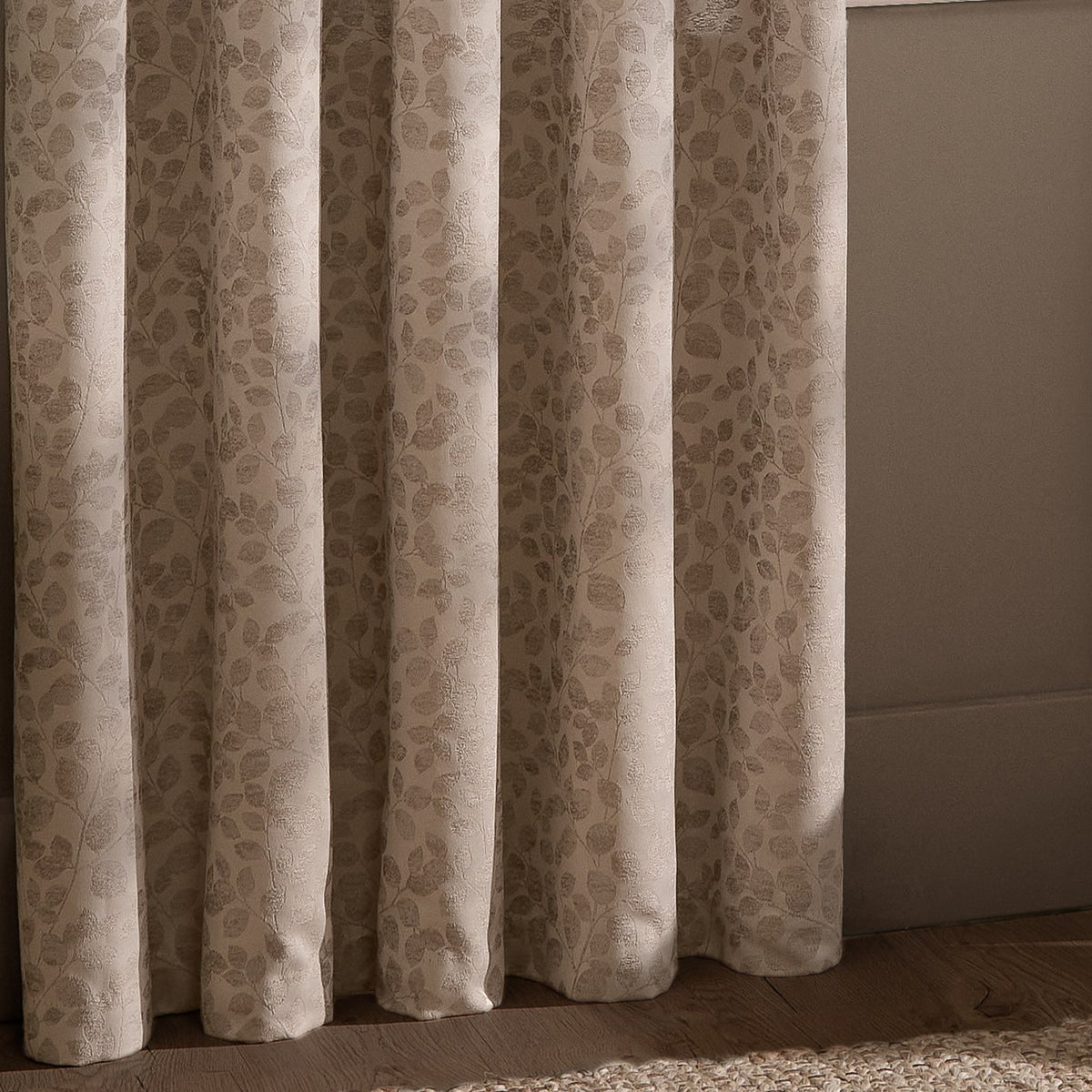 Grace Leaf Jacquard fully lined eyelet curtains in taupe, showing draped folds with a woven leaf pattern in a bedroom setting.