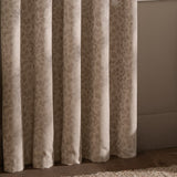 Grace Leaf Jacquard fully lined eyelet curtains in taupe, showing draped folds with a woven leaf pattern in a bedroom setting.