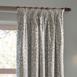 Grace Leaf Jacquard pencil pleat curtains in mist grey, showing a woven leaf pattern on pale fabric with pencil pleat heading, hung on a wooden pole beside a window.
