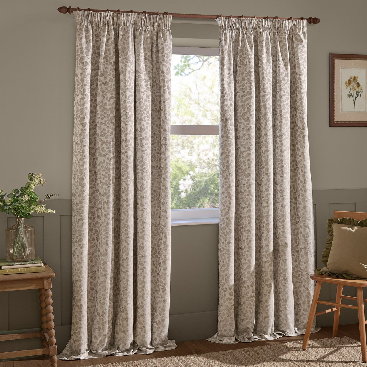 Grace Leaf Jacquard pencil pleat curtains in natural beige with a woven leaf pattern, hung on a wooden pole beside a window in a living room.