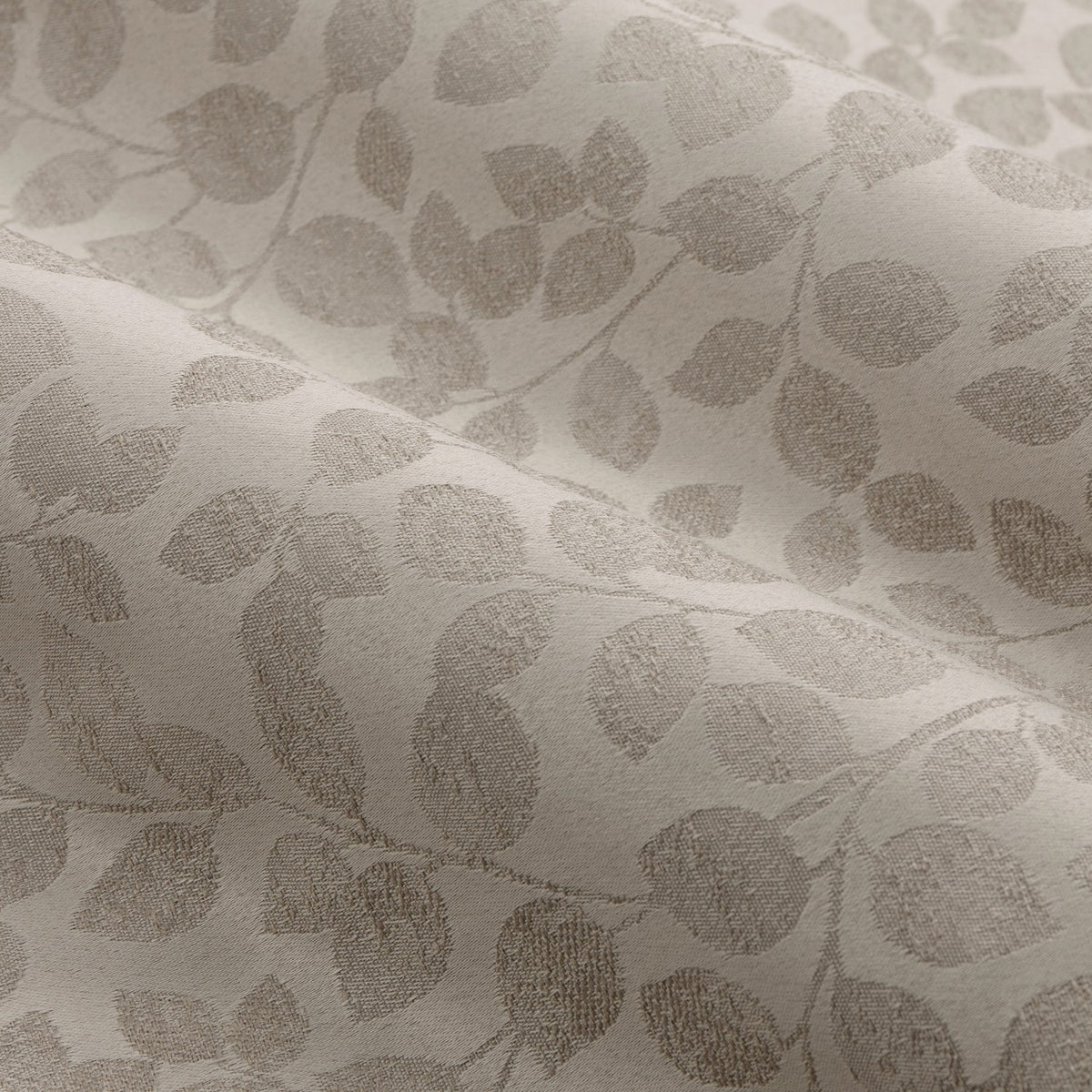Close-up of Grace Leaf Jacquard pencil pleat curtain fabric in natural beige, showing a woven trailing leaf pattern on a matt satin polyester ground.